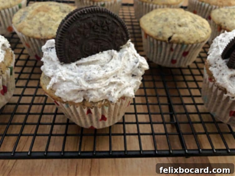 A beautifully decorated Oreo cupcake resting on a cooling rack, alongside undecorated cupcakes.