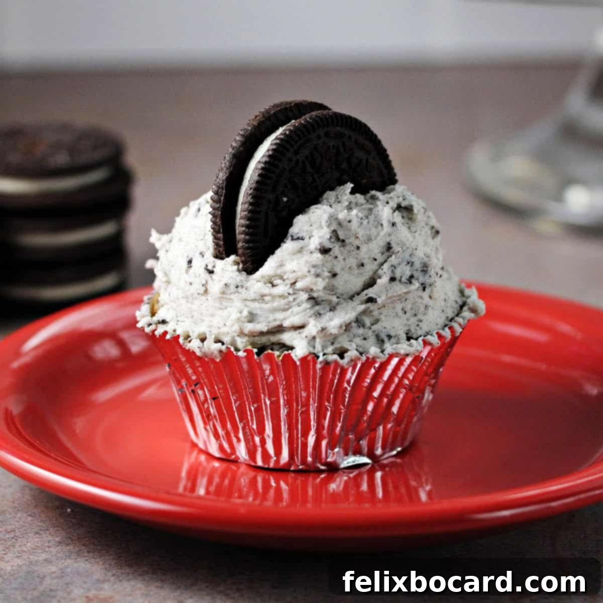 Close-up of a cupcake generously topped with Oreo Buttercream Frosting and garnished with a piece of Oreo cookie, served on a vibrant red plate.