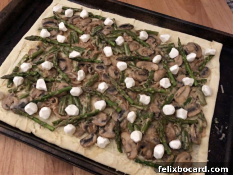 Puff pastry galette base dotted with pieces of fresh mozzarella cheese before baking