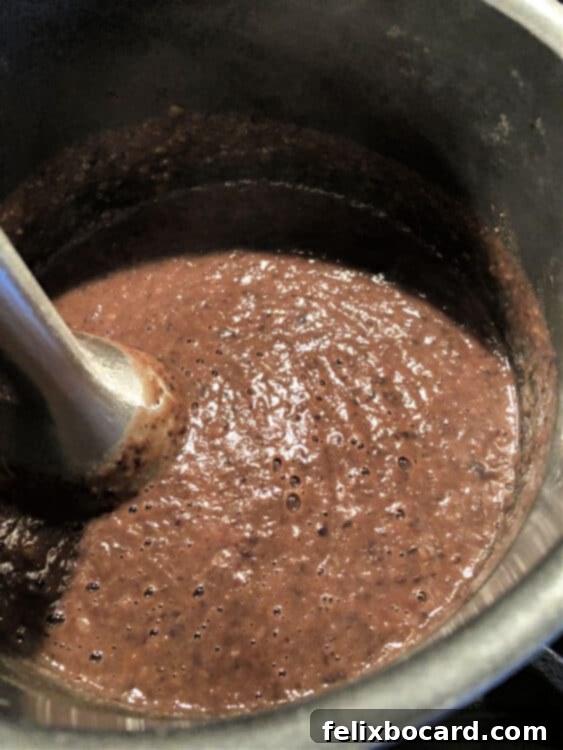 An immersion blender is actively blending the black bean soup in the pot, transforming it into a smooth, creamy texture.