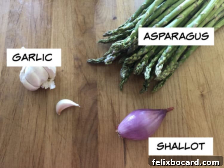 Fresh asparagus spears, a shallot, and garlic cloves arranged on a cutting board, ready for pan frying.