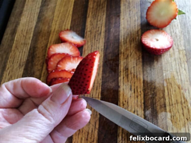 Close-up showing a freshly cut strawberry slice, highlighting the precise angled cut that creates a perfect oval, ideal for the detailed footpads of bunny butt pancakes.