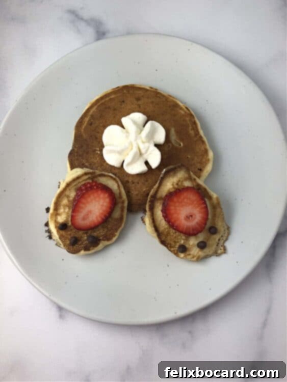 A perfectly assembled bunny butt pancake on a white plate, showcasing a large round pancake body, two oval pancake feet, strawberry footpads, and a generous dollop of whipped cream as the fluffy tail.