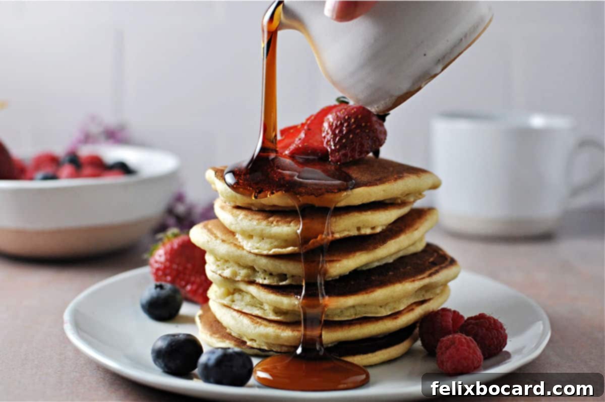A tall stack of golden-brown almond milk pancakes, generously topped with fresh berries and a drizzle of rich maple syrup, ready to be enjoyed for a delicious breakfast.