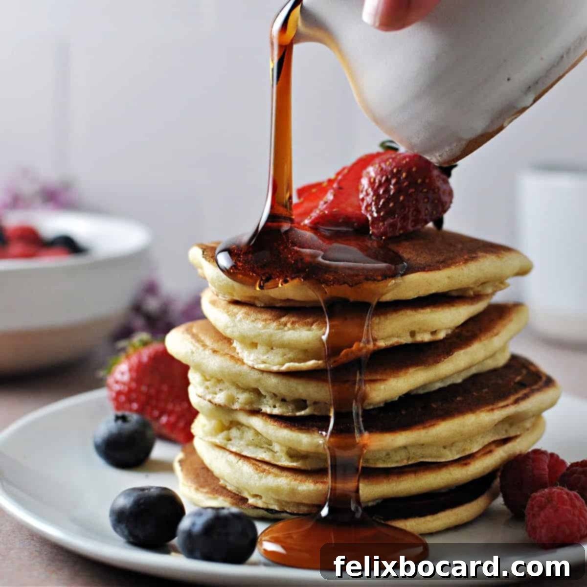 A beautifully composed image of a stack of fluffy almond milk pancakes, garnished with a vibrant mix of fresh berries and a generous cascade of golden maple syrup being poured over the top, making them irresistible.