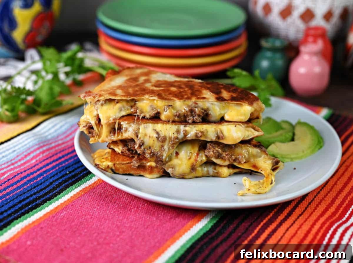 Ground beef quesadilla slices stacked on a plate with the melted cheese oozing out the sides.