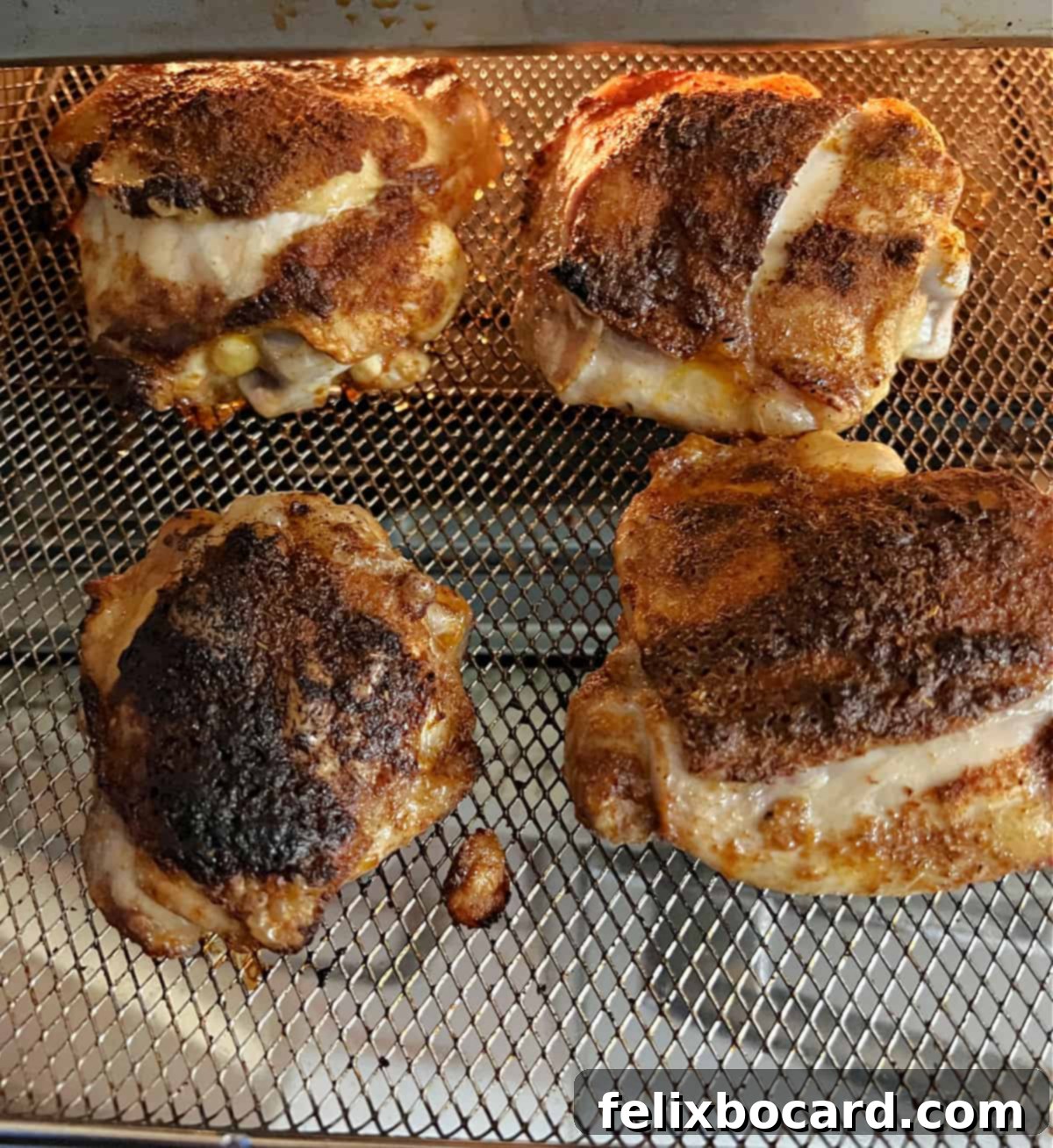 Four chicken thighs partially cooked in an air fryer basket, with golden-brown skin forming.