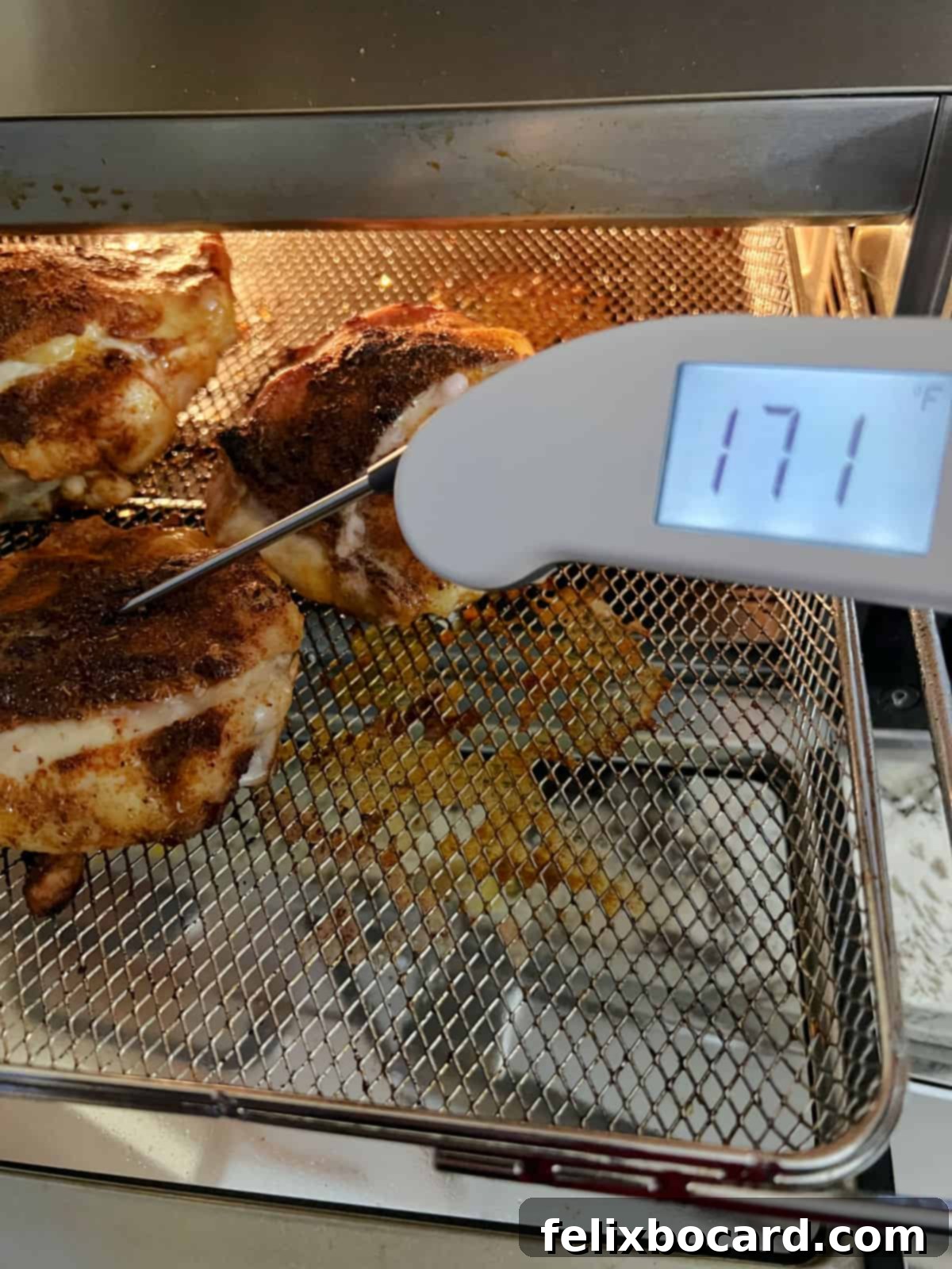 A hand holding a meat thermometer, checking the internal temperature of an air-fried chicken thigh in the basket.
