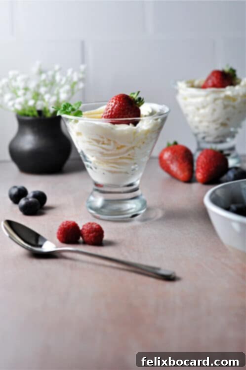 Keto cheesecake fluff piped into a glass and garnished with a fresh strawberry, with additional berries and a second serving in the background.