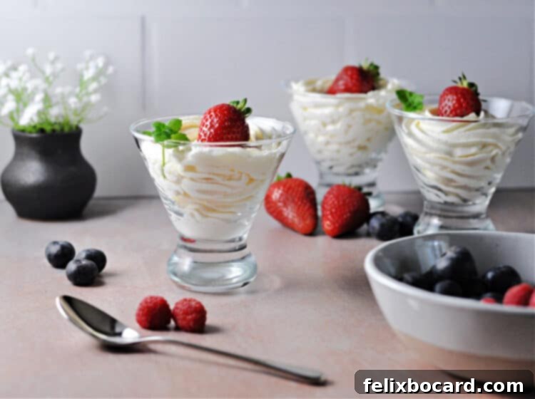 Three glasses of keto cheesecake fluff garnished with vibrant strawberries, arranged beautifully on a table with additional fresh berries scattered around.
