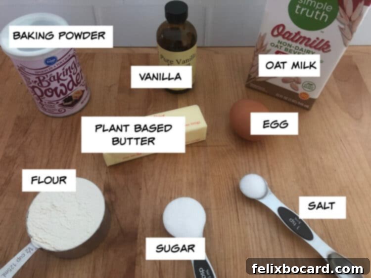 Collection of oat milk pancake ingredients: oat milk carton, stick of butter, fresh egg, container of baking powder, bottle of vanilla extract, bag of flour, bowl of sugar, and a salt shaker.