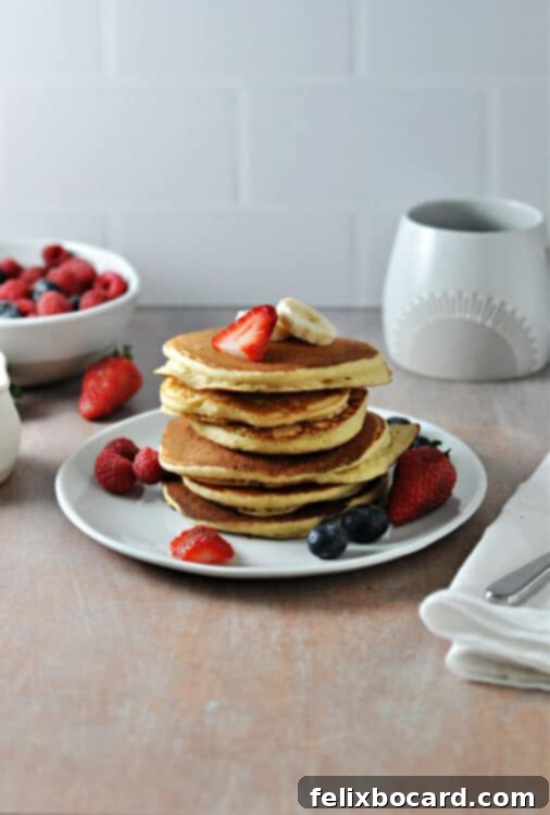 Plate of perfectly cooked oat milk pancakes, garnished with fresh raspberries and blueberries, ready to be served.